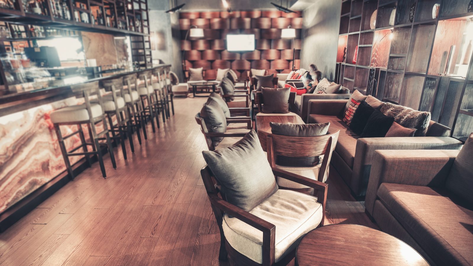 A long lit bar with stools down one side and separate seating groups facing it
